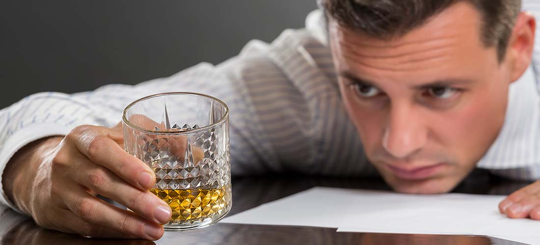 мужчина сидит за столом и смотрит на стакан с алкоголем в своей руке