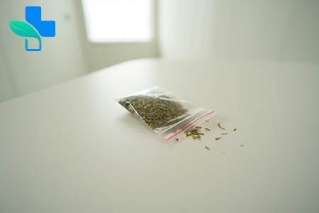 На столе лежит открытый зип пакет с травой