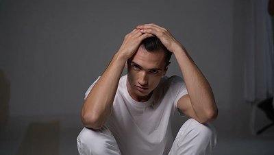 Мужчина сидит на кровати и держится за голову