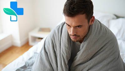Мужчина сидит на кровати накрытый одеялом